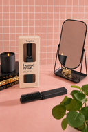 Vogsion black mini heated brush displayed on a pink vanity with packaging, mirror, candle, and hair accessories, ideal for travel-friendly dry hair styling and quick touch-ups.