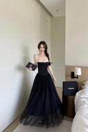 A woman stands in a bedroom wearing Vogsion Petite Structured Lace Corset Tulle Maxi Dress. She is holding a black Chanel box, with a black Chanel shopping bag on the bedside table.