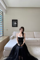 A woman wearing a Vogsion Petite Structured Lace Corset Tulle Maxi Dress sits on a white sectional sofa in a modern living room.