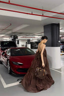 Woman in Vogsion Seraphina Tiered Chantilly Lace Maxi Dress - Romantic Pastel Coquette Gown holding a handbag in a parking garage with a red car and pipes.
