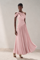 A model wearing a light pink Vogsion Signature Pleated Draped Shoulder Dress in Ivory/ Light Pink, paired with metallic sandals, set against a neutral studio backdrop.