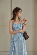 Editorial portrait of the Vogsion Sky Mist Blue Ruffle Maxi Dress in soft natural daylight. Flowing blue floral chiffon with cascading ruffles, matching full lining to reduce transparency, elegant maxi length, ideal for wedding guests, vacations, and summer celebrations.