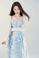 Woman wearing a Vogsion Sky Mist Blue Ruffle Maxi Dress with a white cardigan on a white background