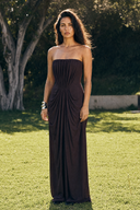 A woman stands outdoors on a grassy lawn wearing a Vogsion Strapless Ruched Maxi Dress - Dark Plum/Chocolate Wedding Guest Evening Gown in a very dark plum or eggplant shade. Trees and shrubs are visible in the background.