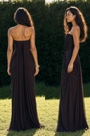 A woman modeling a Vogsion Strapless Ruched Maxi Dress - Dark Plum/Chocolate Wedding Guest Evening Gown gown outdoors, shown from the back on the left and in side profile on the right, against a hedge and grass background.