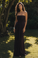 A woman stands outdoors on grass in front of trees, wearing a Vogsion Strapless Ruched Maxi Dress - Dark Plum/Chocolate Wedding Guest Evening Gown with a gathered waist and flowing skirt.