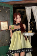 Woman in Vogsion Velvandis Off Shoulder Dot Mini Dress (Sage Green Polka Dot) dress holding a drink and tray in front of a rustic building entrance.