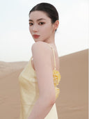 Woman wearing Vogsion x Last Sunset Butter Yellow Satin Backless Slip Maxi Dress with Rosette Detail with floral details against a neutral background