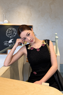 Upper-body view of a black textured knit dress with purple floral beads and gold-tone neckline accents.