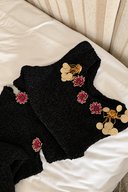 Black textured knit dress laid on a cream seat, showing purple floral beads and gold-tone hanging disc embellishments.