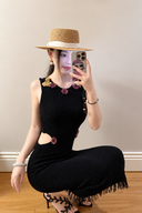 Long version of the black embellished knit dress with a side waist cutout and fringed hem, styled with a straw hat; not the mini-length version.