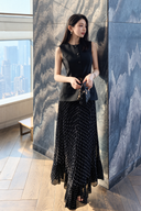 Full-length view of a black two-in-one dress with an attached vest-style bodice, white polka-dot pleated skirt and included belt.