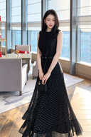 Front view of the black polka-dot pleated dress, showing its sleeveless vest-style upper section and belted waist.