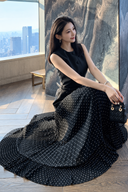 Seated view of the black two-in-one dress with its white polka-dot pleated skirt spread out to show the folds.