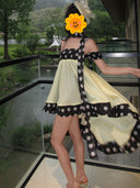 Woman wearing Vogsion Velvandis Off Shoulder Dot Mini Dress (Sage Green Polka Dot) with a yellow flower over her face, standing on a balcony with a scenic background.