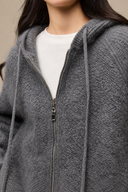 Grey cardigan close-up showing fine fuzzy fibres, textured knit, hood drawstrings and metal zipper details.