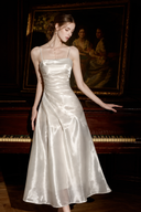Model resting one hand on a piano in the Isabeau ivory draped satin maxi dress.