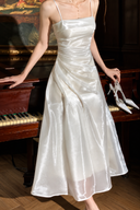 Close-up of the Isabeau ivory satin dress showing its folded neckline, ruched bodice and draped waist beside a piano.