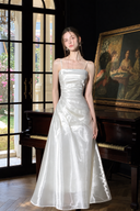 Full-length window-light view of the Isabeau ivory satin maxi dress and flared skirt.
