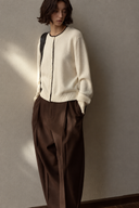 Ivory wool cardigan with contrast neckline trim and brown pleated trousers