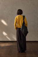Back view of yellow wool cardigan with ribbed hem and a dark shoulder bag