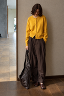 Yellow crewneck wool cardigan with ribbed cuffs, worn with pleated brown trousers