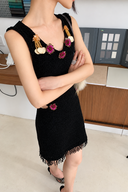 Close view of the black knit mini dress showing textured knit, fixed floral beadwork and gold-tone neckline decorations.