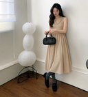 Beige cotton knit midi dress with matching flower detail, full-length model view beside a paper floor lamp.