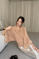 Seated model in a blush cowl-neck sweater with a ribbed hem and rabbit-fur sleeve trim, paired with an ivory satin skirt