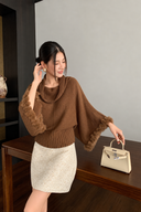 Brown batwing knit sweater with a draped cowl neck and fitted ribbed hem, paired with an ivory textured mini skirt