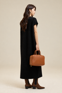 Back three-quarter view of the black knit dress styled with brown ankle boots and a tan leather bag.