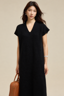 Front detail of a relaxed black V-neck sweater dress with short cap sleeves and a tan bag.