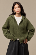 Front view of a Sage Green wool, mulberry silk and cashmere hooded cardigan with a two-way zip, styled with black wide-leg trousers.