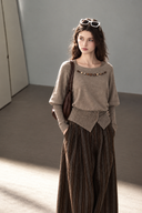 Taupe beaded boatneck cotton knit top with contrast sleeves and buttoned waist, styled with pinstripe trousers.