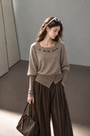 Front view of a taupe beaded cotton knit top with a fitted contrast waistband and layered sleeve detail.