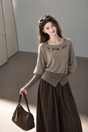 Taupe layered-look cotton knit top with embellished boat neckline, worn with a brown handbag and pinstripe trousers.