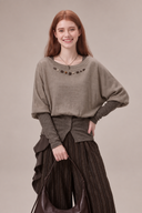 Studio view of a taupe layered-look cotton knit top with decorative beads and a buttoned contrast hem.