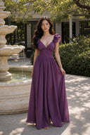 Purple wedding guest maxi dress with deep V neckline beside a garden fountain