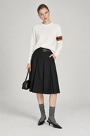 Woman wearing Aveline ivory wool crewneck sweater with a black pleated skirt