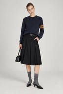 Woman wearing Aveline navy wool crewneck sweater with caramel sleeve stripes and a black pleated skirt