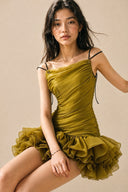 Seated view of the olive green mini dress with a voluminous petal-shaped ruffle hem