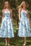 Two front views of the VOGSION Bluebell Garden blue and white floral midi wedding guest dress with a ruffle-trim neckline