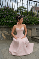     Vogsion Roselle Blush Floral Corset Lace-Trim Midi Dress worn outdoors by a customer in a garden setting with pink floral print and sweetheart neckline