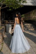 Back view of the Vogsion Célestine icy blue open-back maxi dress with delicate straps, black trim, and a flowing chiffon-style skirt for resort wedding and vacation styling.