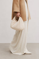 Woman carrying the VOGSION Cloudshell Convertible Mini Hobo Bag in Creamy with a minimalist neutral outfit.