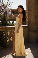 Side view of the Vogsion Cyra Asymmetrical Draped Maxi Dress in butter yellow with a sculpted strapless corset, elegant asymmetrical ruching and flowing maxi silhouette.