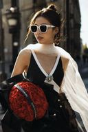 Close-up of a model wearing the Vogsion Éternelle black and white brooch maxi dress with built-in padded cups, white sunglasses, sheer scarf and red roses.