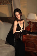 Side detail of the Vogsion Éternelle black maxi dress beside a vintage nightstand, showing its deep V neckline, built-in padded cups and crystal brooch detail.