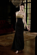 VOGSION black and gold embellished strapless evening maxi dress under a crystal chandelier