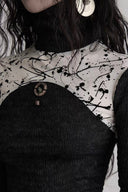 Close-up of the sheer white splatter-print panel and fixed circular ornament on the black Gothic top